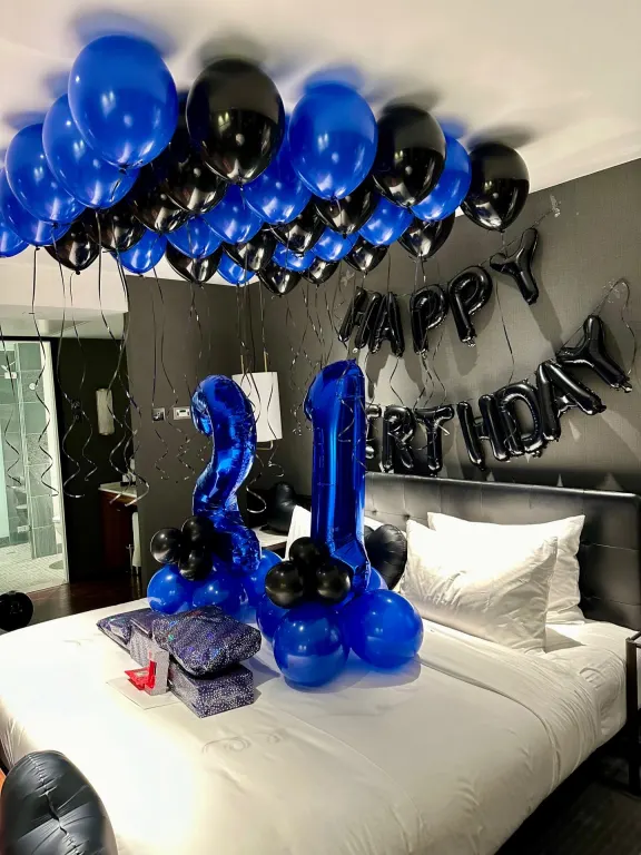 Blue and black balloon ceiling over a hotel bed, with a large blue 21 and Happy Birthday letters