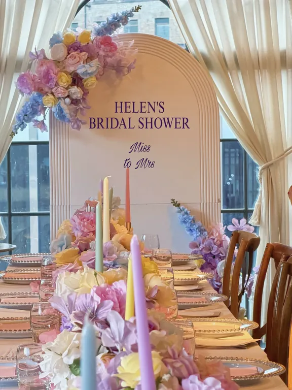 Pastel bridal shower table with tall candles and flowers in front of an arched Miss to Mrs backdrop