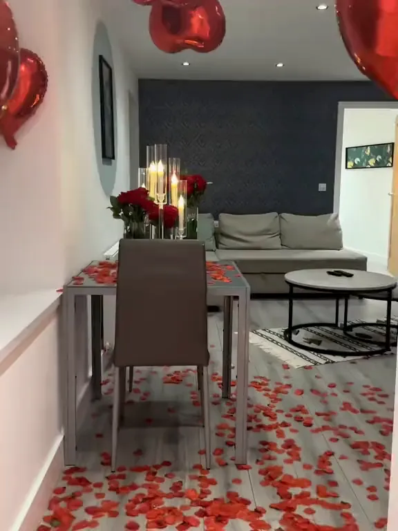 Table for two with red roses and tall candles among rose petals