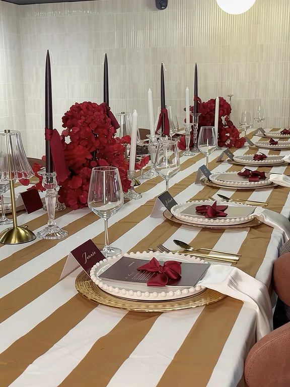 Dinner table with gold striped linen, dark red roses, tall black candles and handwritten place cards