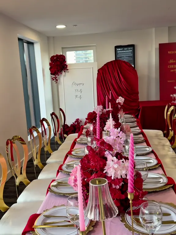 Long dinner table dressed in pink and red with gold chairs, pink candles and a champagne tower behind