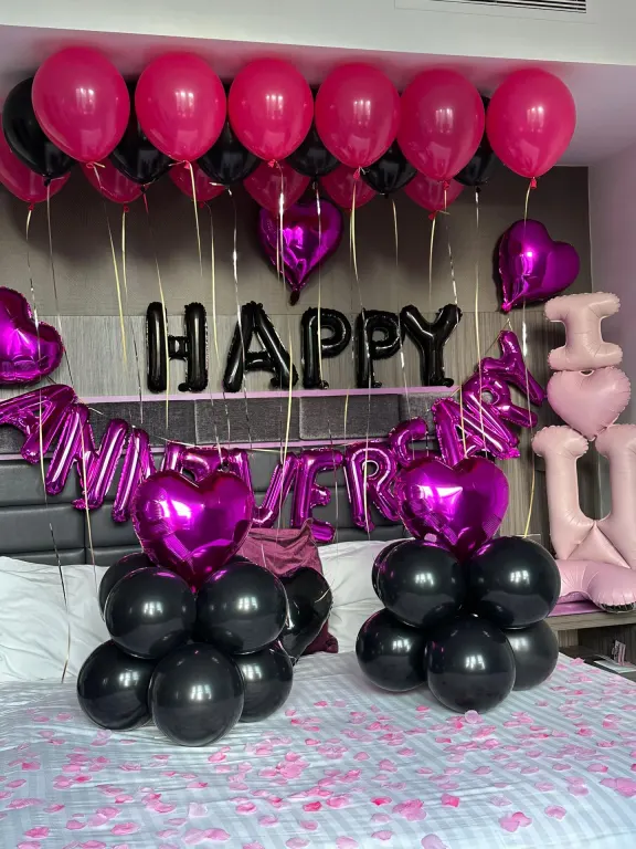 Hotel bed with Happy Anniversary in pink foil letters under pink and black balloons