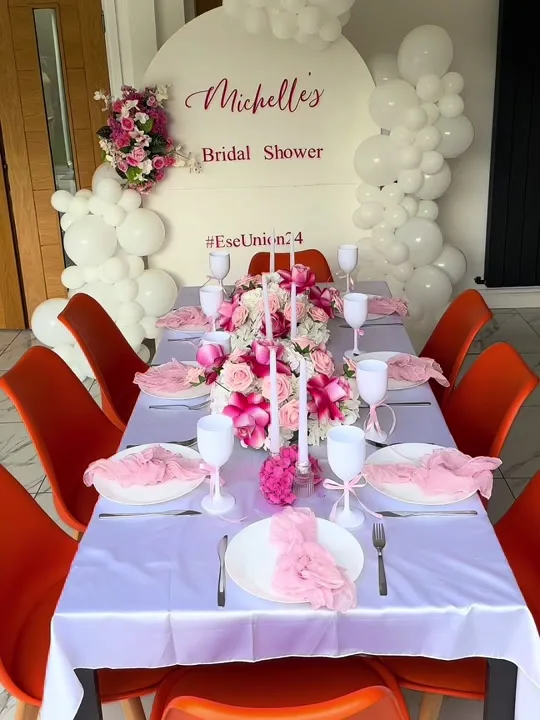 Long table set in pink and white in front of a white balloon arch and a bridal shower backdrop